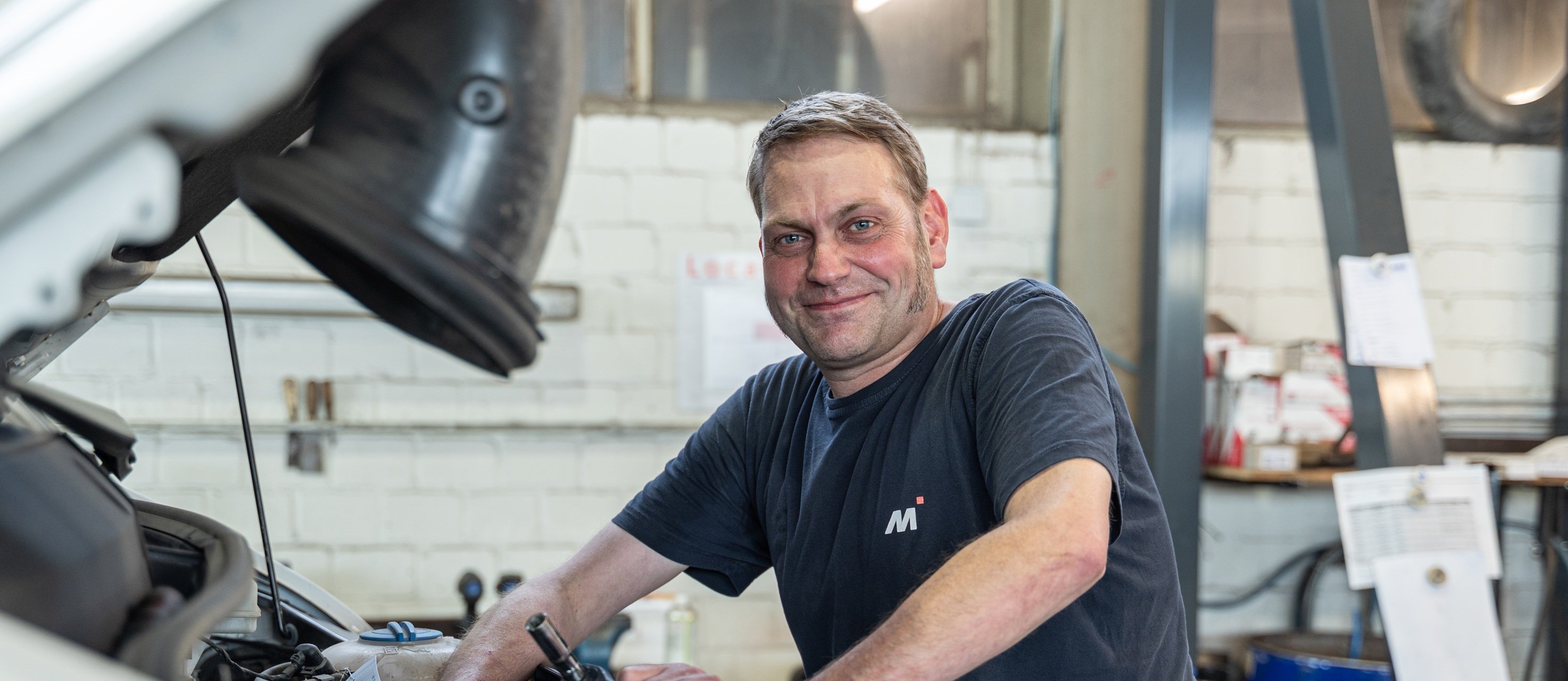Mechaniker arbeitet an einem offenen Motorraum in einer Werkstatt.