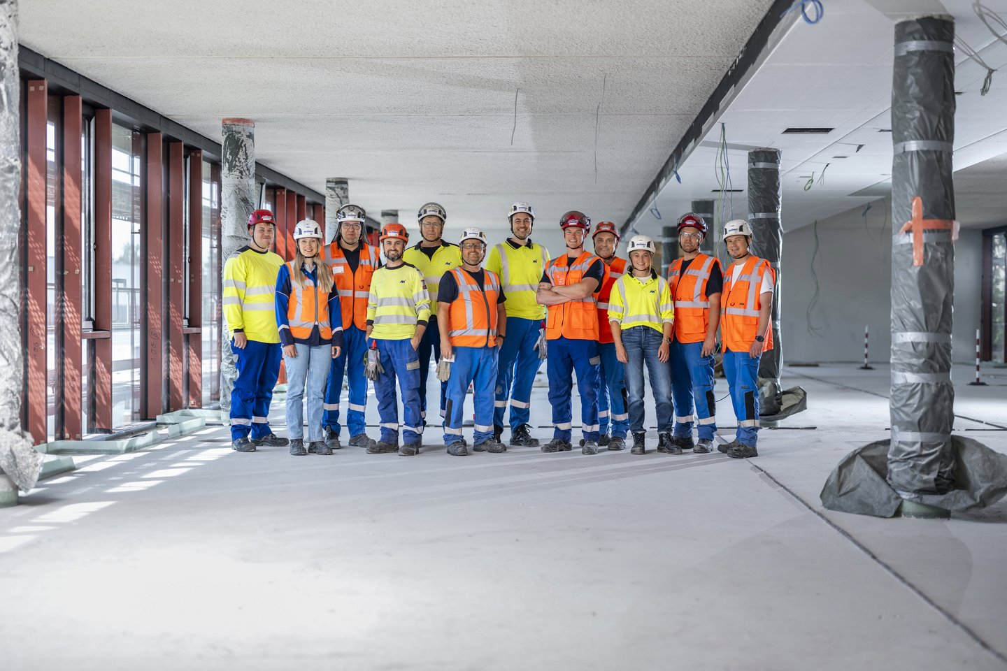 Bauarbeiter arbeiten gemeinsam an neuer Gebäudestruktur Mehrere Bauarbeiter in Sicherheitswesten und Helmen stehen in einer unfertigen Gebäudeetage nebeneinander.